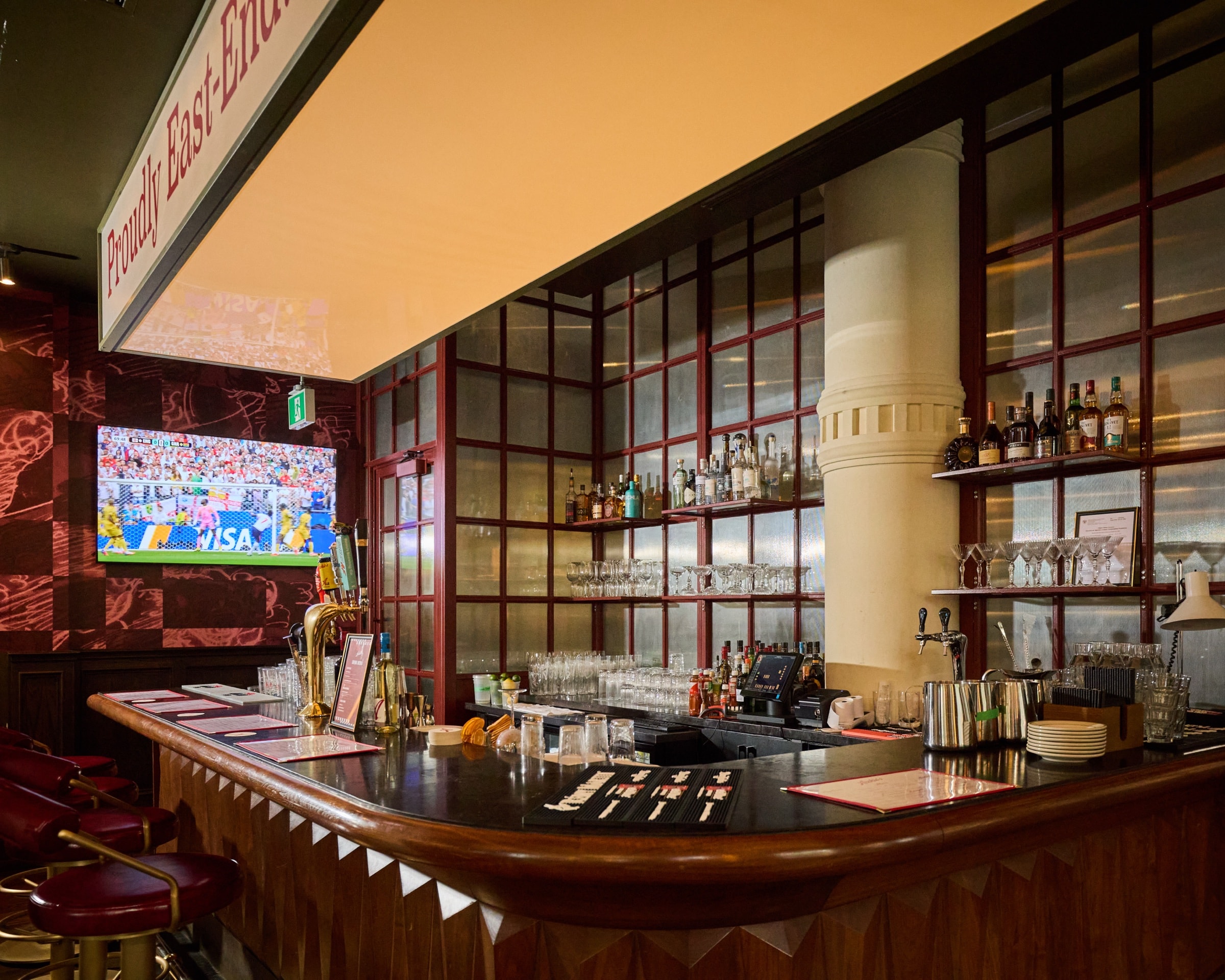 Archie's curved wood bar with red stools, glassware, spirits, beer taps, and a television