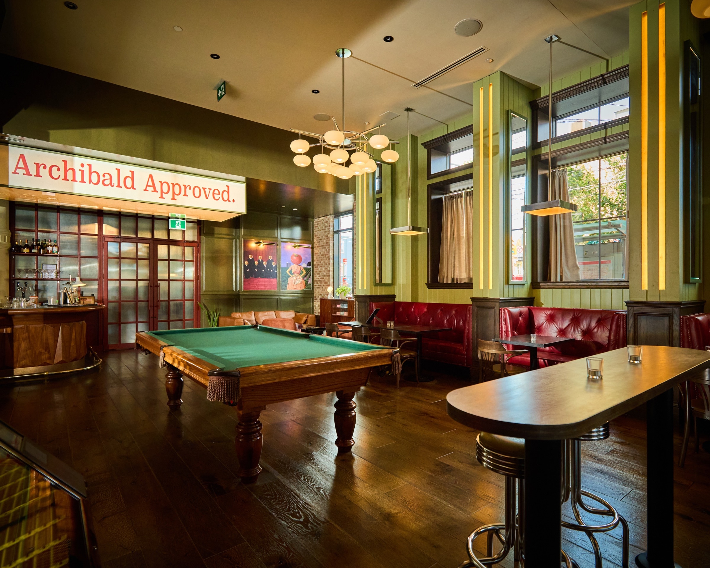 Archie's green pool table surrounded by red banquettes, high-top seating, globe chandeliers, and the bar