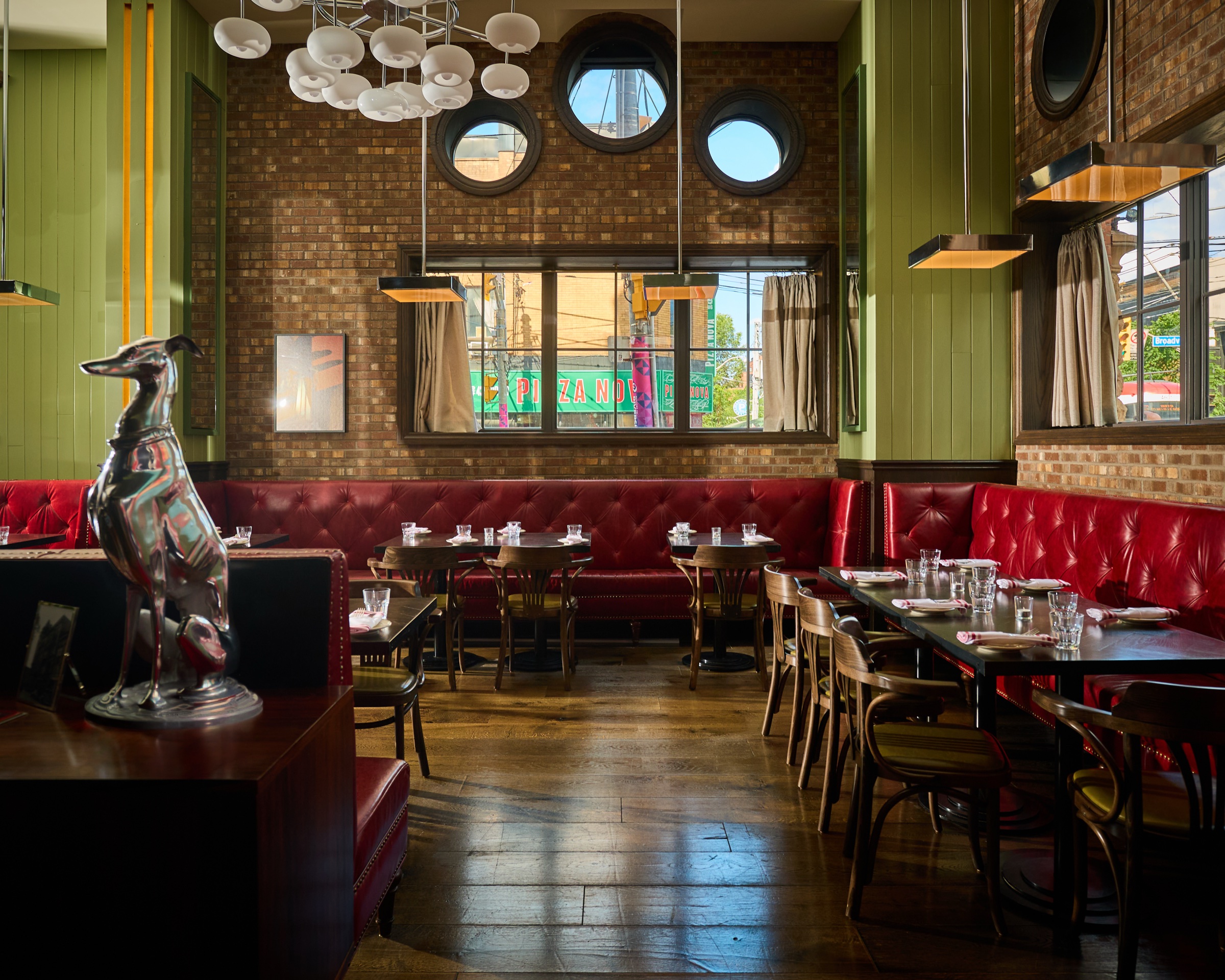 Archie's dining room set with glassware, red leather banquettes, wood chairs, chandeliers, and round windows